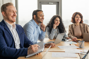 Aufkleber - A group of four business professionals are gathered around a table in a modern office setting. They are engaged in a meeting, listening attentively and taking notes. The atmosphere is positive