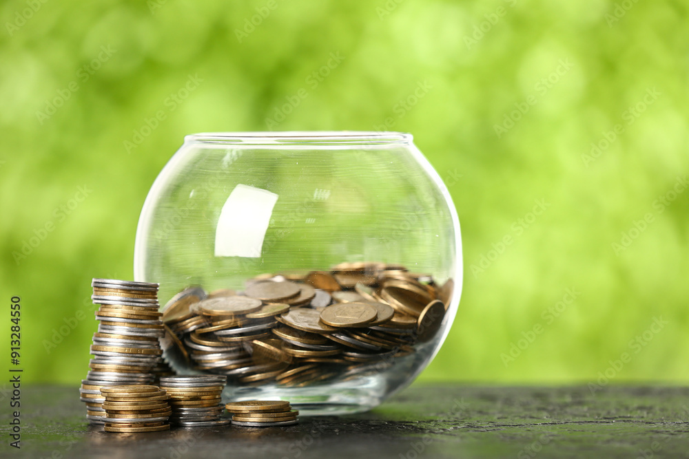 Jar with coins on table against blurred green nature background. Savings concept