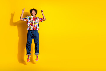 Sticker - Full size photo of nice funky young man jump direct fingers up empty space wear shirt isolated on bright yellow color background