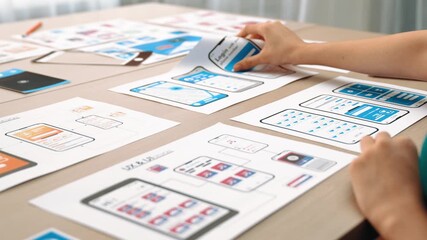 Startup company employee planning for user interface prototype for mobile application or website in office with model of program on desk. UX UI designer consider user friendly interface plan. Synergic
