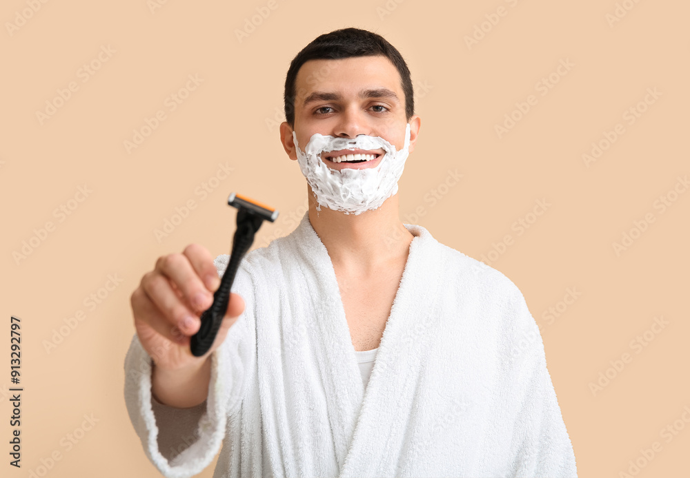 Handsome young man with razor and shaving foam on his face against beige background