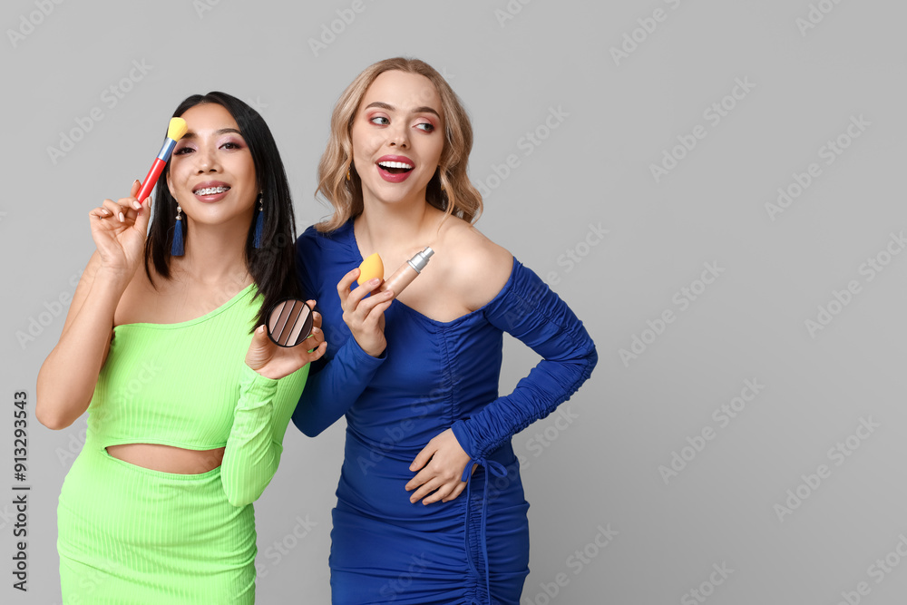 Pretty young women with decorative cosmetic products on grey background