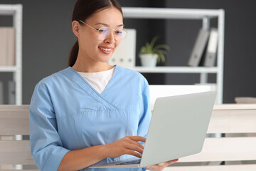 Poster - Young female medical receptionist in eyeglasses with modern laptop in hospital