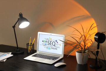 Poster - Workplace with modern laptop, stationery and glowing lamp in stylish office at evening. SEO concept