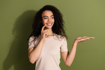 Wall Mural - Photo of adorable girl with wavy hairdo dressed beige t-shirt look at object on palm empty space isolated on khaki color background