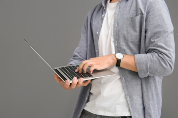 Male programmer using modern laptop on grey background, closeup