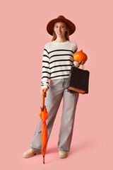 Poster - Young woman in autumn clothes with pumpkin, umbrella and shopping bags on pink background