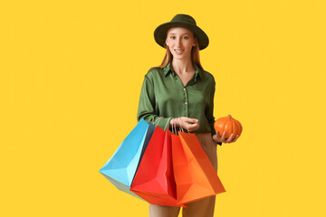 Poster - Young woman in autumn clothes with shopping bags and pumpkin on yellow background