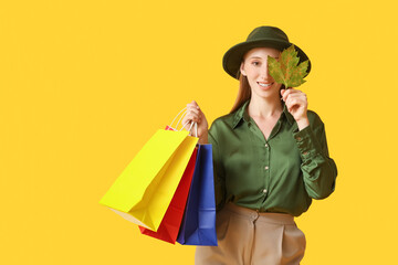 Young woman in autumn clothes with shopping bags and leaf on yellow background