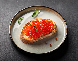 Sandwich with red caviar on a plate on a gray background