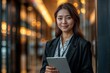 © LAYHONG - A professional woman in a suit holding a tablet, standing indoors with bokeh lighting, exuding confidence and modernity..