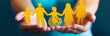 © pikshine - A pair of hands holding yellow paper cutouts representing people, including one person in a wheelchair and another with a child symbol on it. Ensuring Workplace Inclusivity through Diverse Hiring