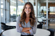 © GraysonStock - A young businesswoman standing with her arms folded in a meeting room, smiling and looking straight ahead, a working woman
