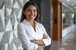 © GraysonStock - Latina businesswoman in white shirt, standing with arms crossed smiling, female manager in modern office.