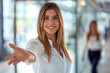 © GraysonStock - A businesswoman extending her hand, welcoming a person to a company, smiling and looking at the camera.
