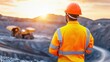© ParinApril - A construction worker watches a sunset over a mining site, showcasing safety gear and the beauty of the industrial landscape.