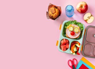 Wall Mural - School lunch box for kids with food in the form of funny faces. School lunch box with sandwich, vegetables, water and stationery on table. Healthy eating habits concept. Back to school concept