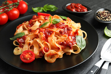 Delicious pasta with tomato sauce, vegetable, basil and spices served on dark textured table, closeup