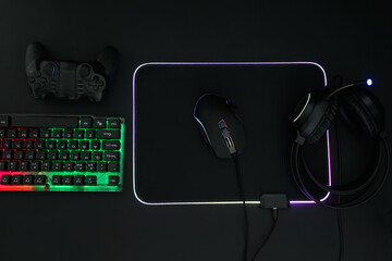 Wall Mural - Computer mouse, headset, RGB keyboard and game controller on black background, flat lay