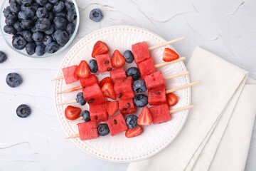 Wall Mural - Skewers with tasty watermelon, strawberries and blueberries on white textured table, flat lay