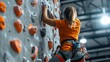 © busro - Active young female climber in sportswear climbing up an artificial rock wall, with a clear view of her technique and climbing equipment from behind