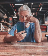 Sticker - Serious bearded senior white-haired man sitting at cafe table using mobile phone reading unpleasant news