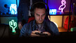 © Krakenimages.com - Focused man wearing headphones plays console games in a colorful illuminated gaming room at night.