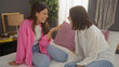 © Krakenimages.com - Two smiling women, likely hispanic, are sitting on a bed having a joyful conversation in a cozy bedroom with decor, showcasing a warm interior home setting.