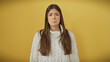 © Krakenimages.com - A perplexed young hispanic woman stands against an isolated yellow background, emoting confusion.