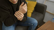 © Krakenimages.com - Man suffering from wrist pain while sitting on a couch at home, indicating discomfort and health issues.