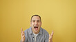 © Krakenimages.com - Excited hispanic man with a surprised expression standing against a yellow background in a casual gray shirt.