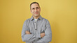 © Krakenimages.com - Portrait of a confident young hispanic man with folded arms, standing against a yellow isolated background.