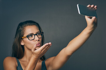 Woman, studio and blow kiss with selfie with glasses on grey background for eyesight and eyewear prescription. Female person, happy and confident with social media post or profile picture with frame