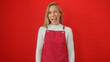 © Krakenimages.com - A cheerful young woman in a red apron winks playfully against a vibrant red background, exuding a fun and lively vibe.