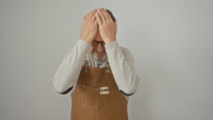 Canvas Print - Stressed senior man in an apron covers his face with hands against a white background.