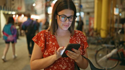 Canvas Print - Beautiful hispanic woman in glasses, smiling and using smartphone on lively shinsekai street, osaka at night