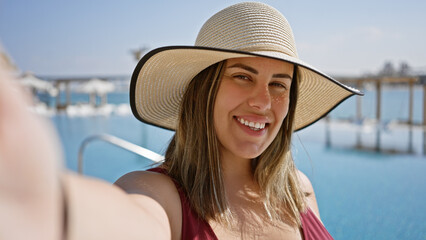 Wall Mural - A smiling woman in a sunhat enjoys a sunny day at a luxury pool with a sea view.