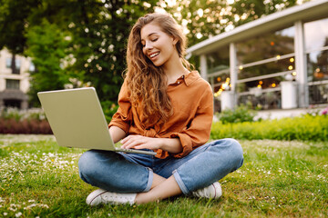 Wall Mural - Young woman sits in park communicating by video call. Girl speaking looking at laptop computer, online conference distance office chat, virtual training concept. Freelancer, Online education.