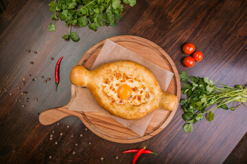 khachapuri with sulguni cheese, herbs and egg on a wooden surface. Georgian pie. Georgian pizza
