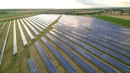 Aerial flyover footage of solar panel photovoltaic energy farm in a green farmland field. High angle shot of pv cells array ssytem generating electricity on a rural summer afternoon. Renewable concept