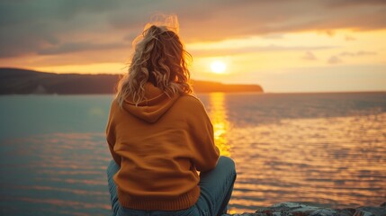 Woman in Orange Hoodie Watching a Serene Sunset by the Sea