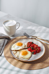 Breakfast with fried eggs and fried tomatoes with spinach on plate and cup of latte coffee