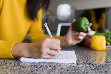 Latin adult woman cooking and writing recipe in a notebook in kitchen at home in Mexico, Hispanic female preparing mexican food in Latin America	