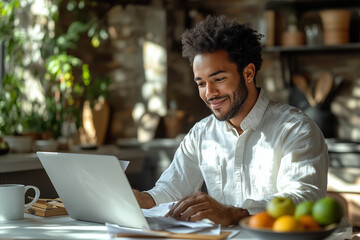 A happy man sits at a white kitchen table with his laptop, looking into an envelope in front of him and smiling to himself. The background is a modern minimalist style home interior. There is also fr