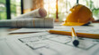 © jex - A close-up of blueprints and pencils on a table, with a construction helmet in the background.