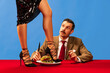 © Lustre Art Group  - Stylish woman in heels pours liquid into glass from above, while man in suit sits at red table with burger, looking up in surprise. Concept of food services, beauty, sales, fashion and style, vintage.