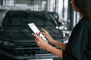 Wireless device, holding digital tablet. Saleswoman in car showroom, selling automobile