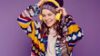 © GraysonStock - A teenage girl dressed in a colorful sweater and a wool cap listening to music with yellow headphones, smiling and happy.
