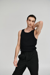 A man in a black tank top poses with his hand on his neck, standing against a white backdrop.