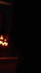 Wall Mural - Vertical video. A Long-Haired Woman in a Dark Room Holds a Jack-O'-Lantern Pumpkin in Front of a Mirror. Halloween Ritual.